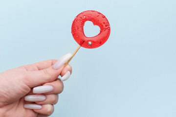 Woman female hand holding heart shaped lollipop on blue background.