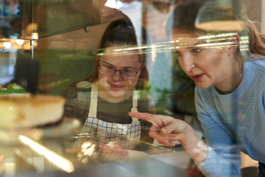 Cafe owner with down syndrome helping customer to order cake in coffee shop