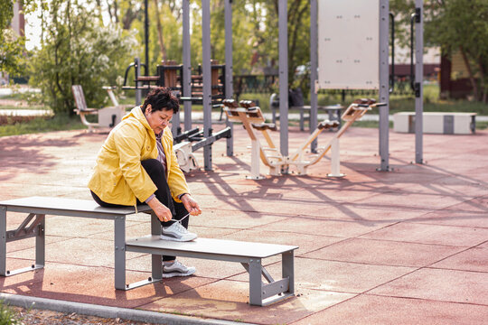 Senior Woman Tying Shoelace Sitting On Bench At Park