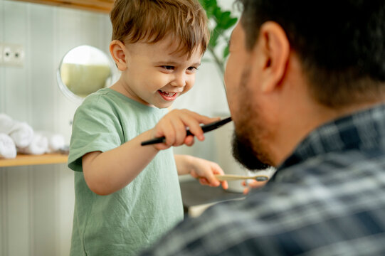 Happy boy brushing teeth of father at home