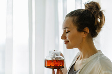 Smiling woman with eyes closed smelling freshly brewed tea at home