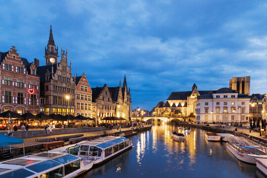 Belgium, East Flanders, Ghent, Historic houses along Graslei,Korenleiand Lys river at dusk with tourboats in foreground