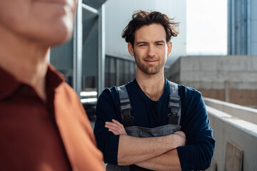 Smiling man in dungaees with arms crossed standing by colleague