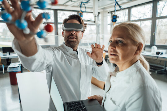 Scientist wearing virtual reality simulator examining molecular structure with colleague