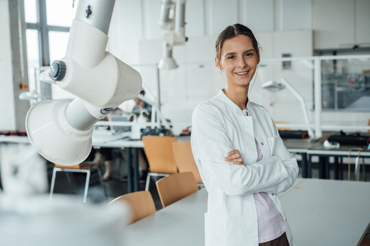Happy young scientist standing by robotic arm