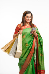 Young Indian woman wearing saree, holding shopping bags and using smartphone.