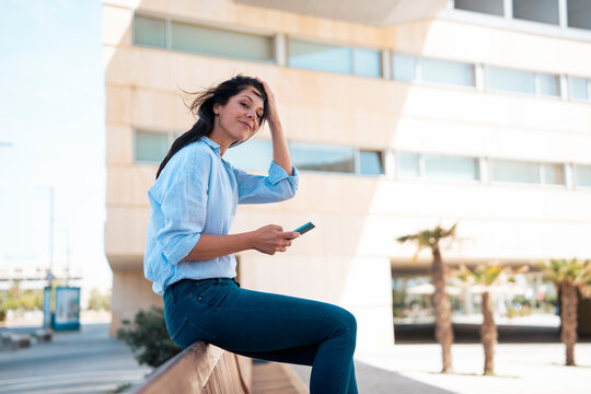 Smiling businesswoman with hand in hair sitting on bench