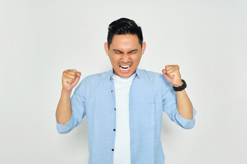 Portrait of angry young Asian man in casual clothes raising hands and screaming with aggressive...