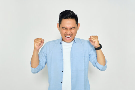 Portrait of angry young Asian man in casual clothes raising hands and screaming with aggressive expression isolated on white background