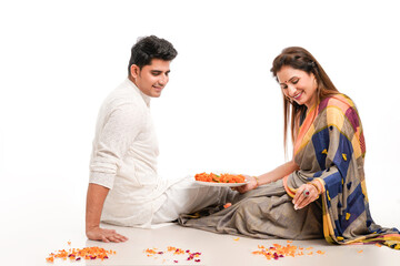 Young indian couple in traditional wear and making flower rangoli.