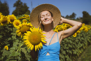 Smiling woman with sun hat holding sunflower in field