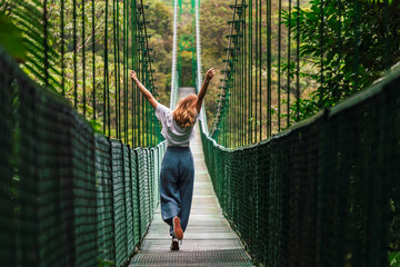 Carefree woman with arms raised spending leisure time walking on suspension bridge