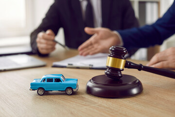 Judge gavel and miniature car symbolize auction or court case against driver who has accident and receiving vehicle insurance payment be on table in front of hands of lawyers. Selective focus