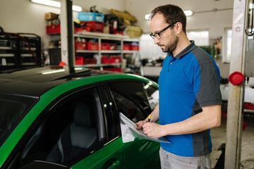 Portrait of male owner of car repair shop. Mechanic detailed vehicle inspection. Auto service centre concept