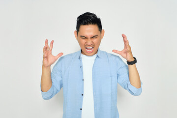 Portrait of angry young Asian man in casual clothes raising hands and screaming with aggressive expression isolated on white background