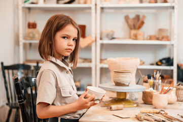 Little girl is indoors with ceramic pot in hands
