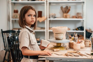 Little girl is indoors with ceramic pot in hands