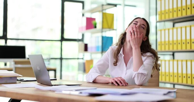 Business woman yawns at office desk in front of laptop. Businesswoman covering mouth out of courtesy chain reaction drowsiness