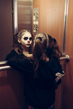 Beautiful 9-year-old gothic girl with sad clown makeup watching herself in the mirror inside the elevator