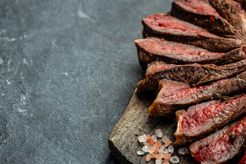 Sliced medium rare grilled steak with red wine on cutting board with rosemary and spices