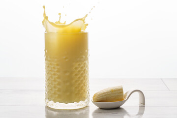 banana milkshake with a natural banana in a white spoon and splash effect splashing drops