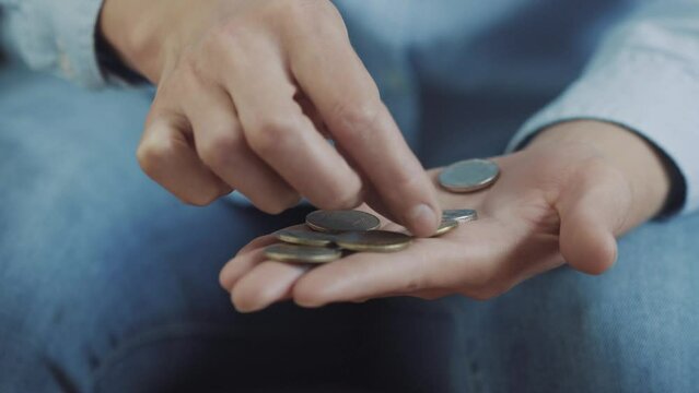 female person counts small coins lying on palmsitting on the sofa