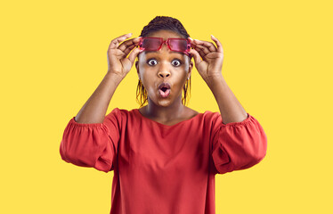 Wow, look at that. Young black girl surprised by unusual situation. Afro American lady sees something extraordinary. Beautiful woman takes off glasses and looks at camera with shocked face expression