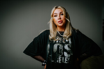 A blonde girl in dark clothes is photographed in the studio on a dark background