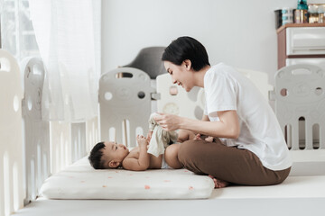 Cute Asian baby wearing clothes by his mother after changing him diaper. Asian family mother’s day concept.