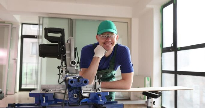 Smiling foreman carpenter working in workshop with circular saw. Professional worker with modern device
