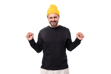 a handsome young 30 year old guy with a beard dressed in a black jacket and a yellow hat hopes with clenched fists