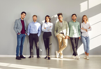 Group of business multiethnic people men and women looking at camera and smiling on gray wall...