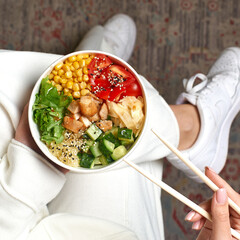 Clean eating diet concept. Chicken bowl with avocado in take out paper container in hands of woman having a lunch break. Close up, copy space, top view
