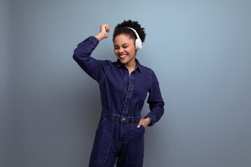 young successful woman with dark skin and black curly hair dressed in a blue denim suit uses...