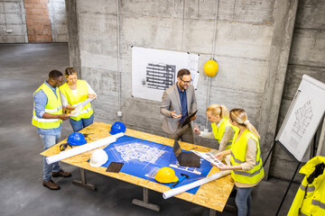 Top view of contractor and architects analyzing plans and blueprints of the new project at...