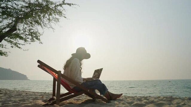 Asian woman typing working on laptop outdoor at sunset on beach, Freelance work