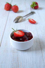 A bowl of strawberry jam on a white wooden table background. Ripe berries.