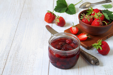 A jar of strawberry jam on a white wooden table background.
