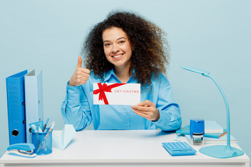 Young employee business woman in casual shirt sit work at white office desk hold gift certificate...