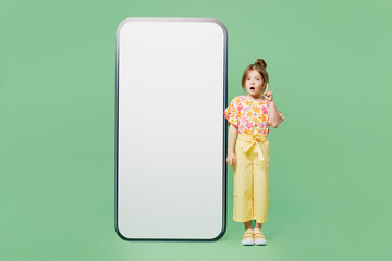 Full body insighted little child kid girl 6-7 years old wear casual clothes big blank screen area mobile cell phone point finger up isolated on plain green background Mother's Day love family concept