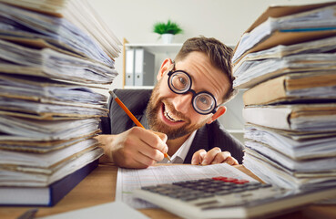 Funny bookkeeper has much paperwork. Crazy man in suit and round glasses sitting at office desk,...
