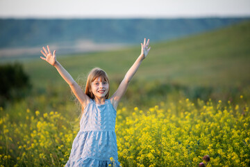 Naklejka na ściany i meble freedom and happiness concept. Happy little girl with hands raised high up in nature
