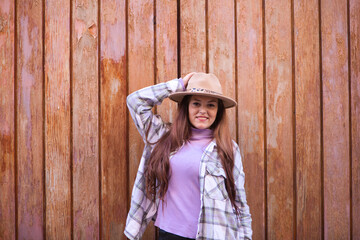 Young and beautiful Spanish woman from Seville with brown hair, hat and checkered shirt standing on a wooden door in different poses and expressions.