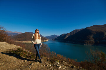 Obraz premium beautiful young woman in sunglasses on the background of a turquoise reservoir and mountains in autumn