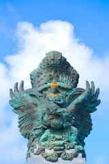 A portrait of Garuda Wisnu Kencana statue, an iconic cultural landmark in Bali, at the GWK Cultural Park with blue sky as background © Radheya Photos