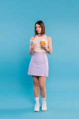 to go coffee, tattooed young woman with short hair and nose piercing holding paper cup and talking on smartphone on blue background, generation z, summer trends, attractive, full length