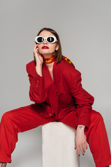 generation z, fashion model with brunette short hair and nose piercing posing in sunglasses and red...