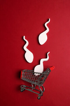 Shopping cart with sperm cells on red background. Sperm  bank and donation concept.