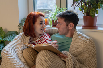 Young family couple man and woman discussing new book while reading together at home, having common interests. Hobbies for couples and intellectual intimacy in relationships concept