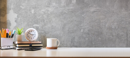 Creative workplace with cup of coffee, clock, potted plant and pencil holder on white table.